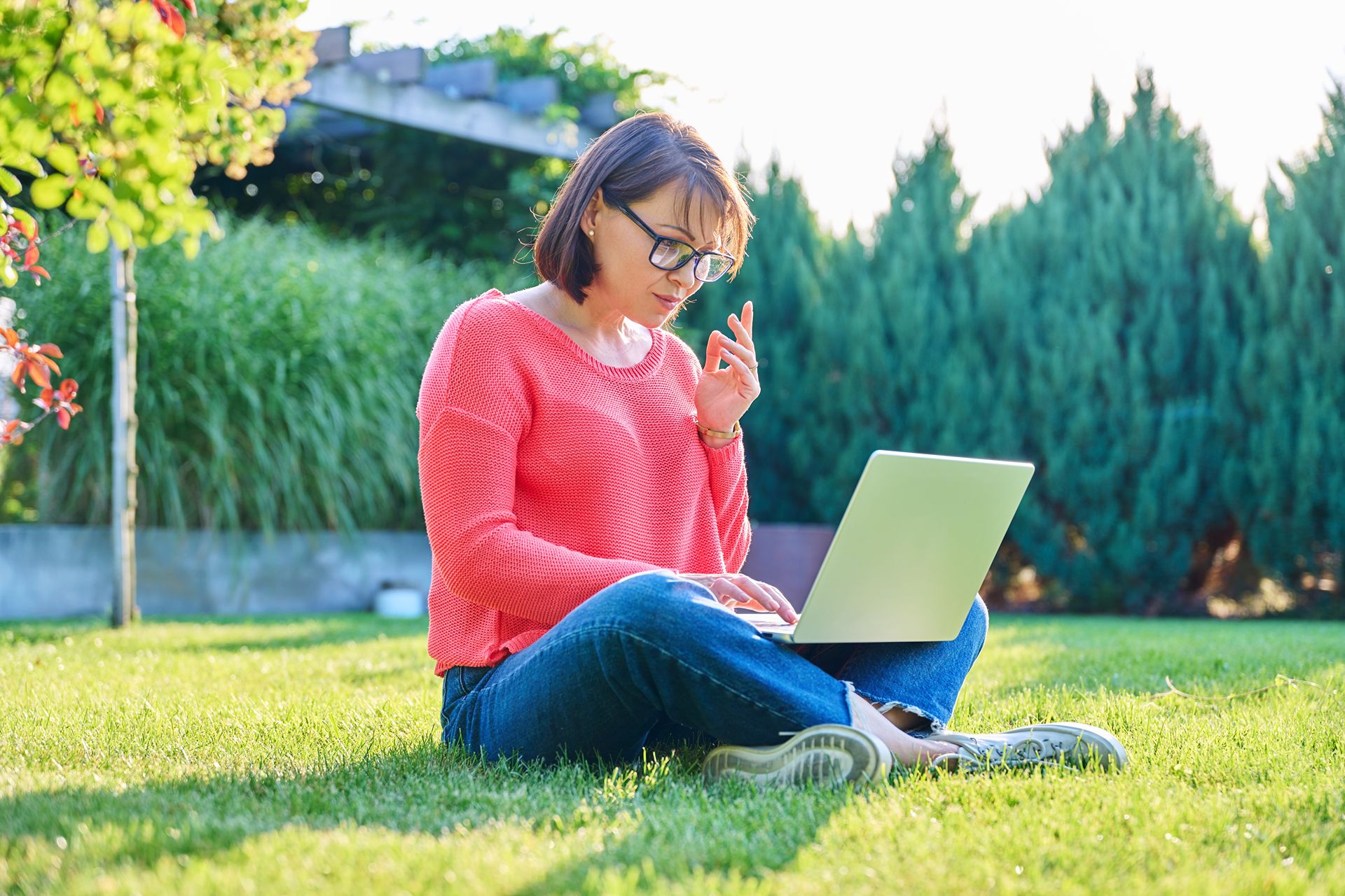 woman sitting in well-landscaped yard with laptop