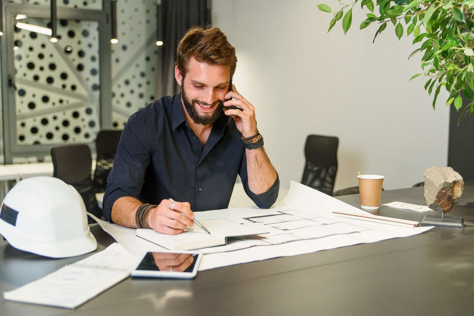 general contractor working on plans at desk while on cell phone
